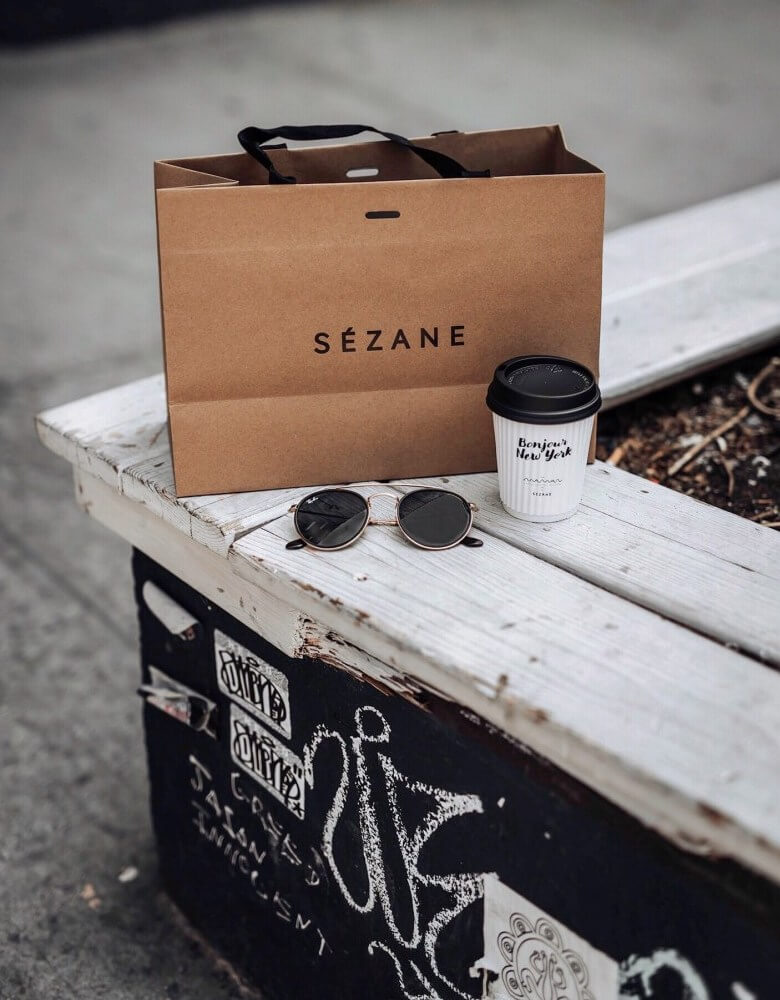 Sac Sézane posé sur un banc avec un café et des lunettes de soleil